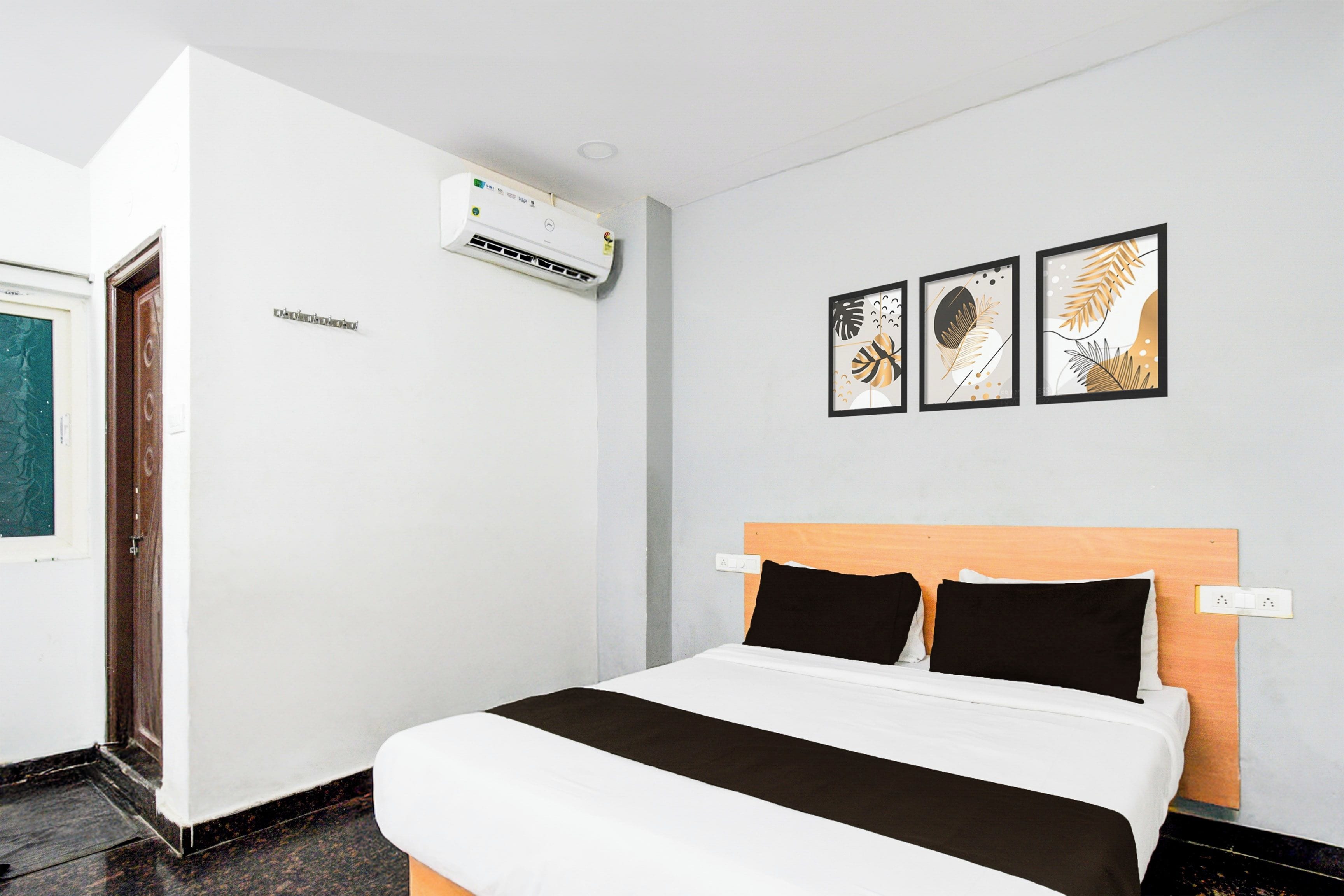 Habitación de hotel con una cama, aire acondicionado montado en la pared y tres obras de arte enmarcadas.