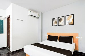 Een hotelkamer met een bed, een wandairconditioner en drie ingelijste kunstwerken.