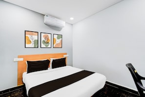 Habitación de hotel con una cama, cabecera, aire acondicionado de pared y tres obras de arte enmarcadas.