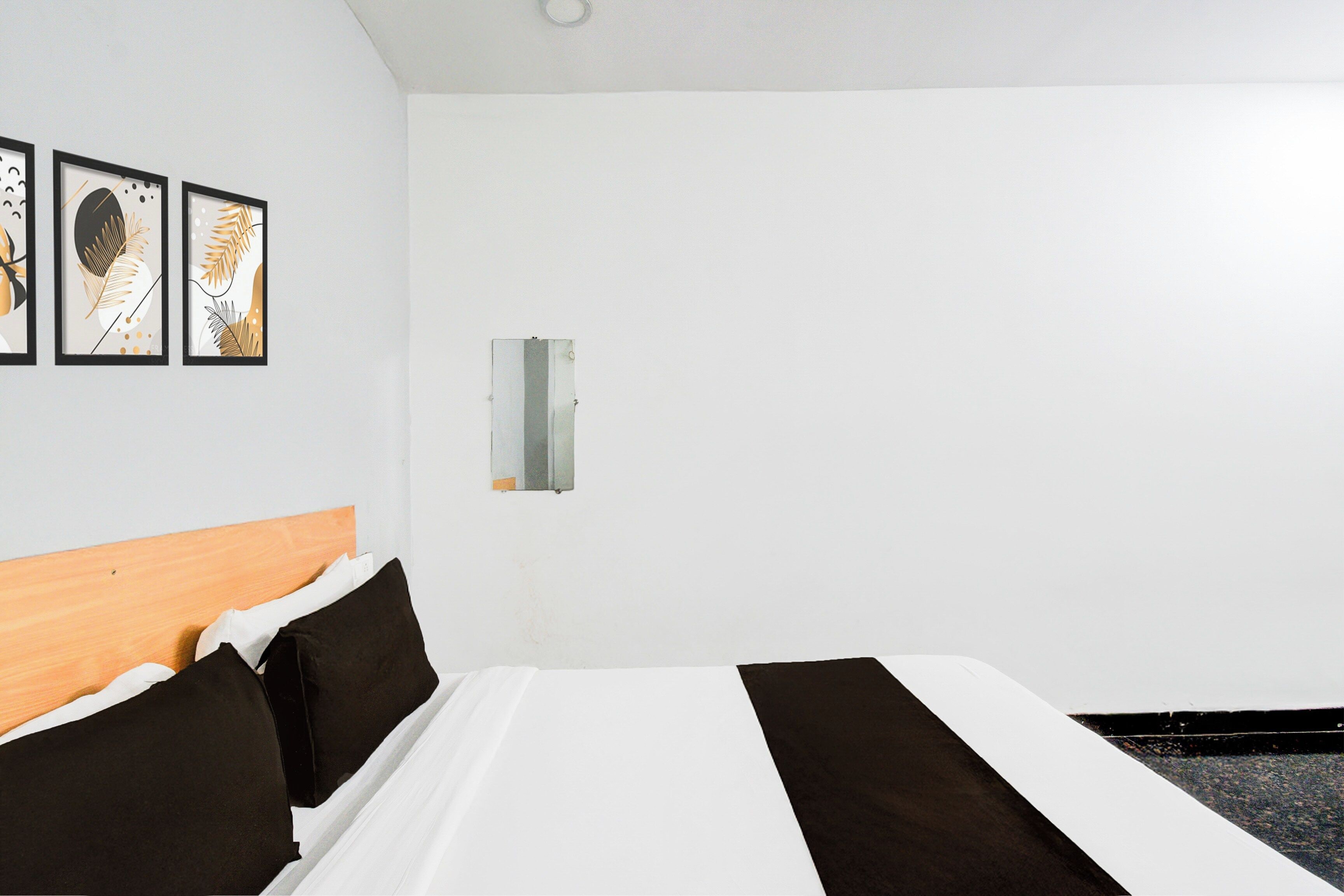 A hotel room with a bed, a wooden headboard, and three framed artworks on the wall.