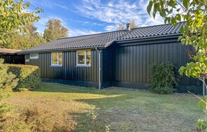 A single-story building with a dark exterior, a tiled roof, and a small front yard with a hedge and a bush. - Nice home in Rønne with WiFi (Rønne)