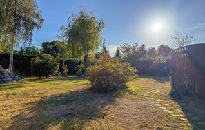 A backyard with a stone pathway leading to a wooden fence, surrounded by trees and a clear sky. - Nice home in Rønne with WiFi (Rønne)