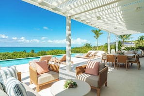 Uma área externa coberta com espreguiçadeiras, piscina e vista para o oceano.