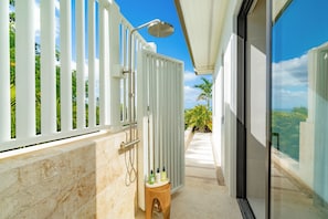 Casa de banho moderna com chuveiro, um banquinho de madeira pequeno e porta de vidro que dá para uma varanda com vista.