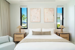Quarto de hotel com uma cama grande, duas mesas de cabeceira, uma cadeira e obras de arte nas paredes.
