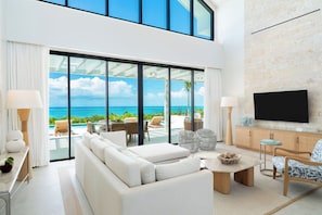 A modern living room with a large sofa, a coffee table, and a TV mounted on a brick wall. - FORGET-ME-NOT (Providenciales)