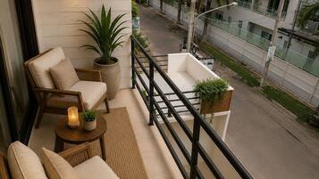 Varanda com mobiliário de vime, planta em vaso e vista para uma rua com edifícios e palmeiras.