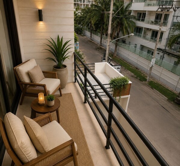 A balcony with wicker furniture, a potted plant, and a view of a street with buildings and palm trees.