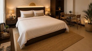 A modern hotel room with a large bed, bedside lamps, a small table with chairs, a potted plant, and a wall-mounted air conditioning unit. - InterCon 3 Bedrooms (Hua Hin)