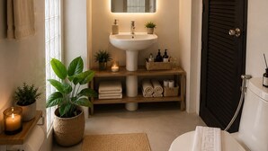 A modern bathroom with a pedestal sink, a mirror above it, a towel rack, a toilet, a dark door, and a small shelf with toiletries. - InterCon 3 Bedrooms (Hua Hin)