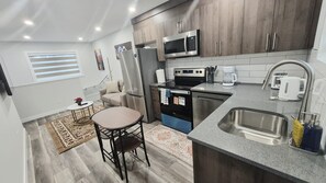 A compact kitchen with a microwave, stove, and sink. There is a small dining area with a table and chairs. - Cozy Laneway Suite in Harbour Landing (Regina)