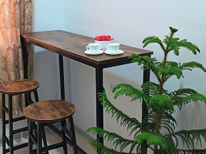 Quarto pequeno com uma mesa de madeira, dois banquinhos e um vaso de planta.