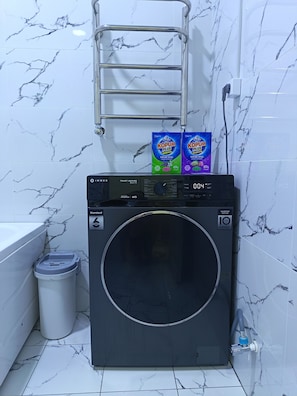 A front-loading washing machine with a digital display, a trash bin, and a metal drying rack above it. - Apartment Valley of legends mall (Namangan)