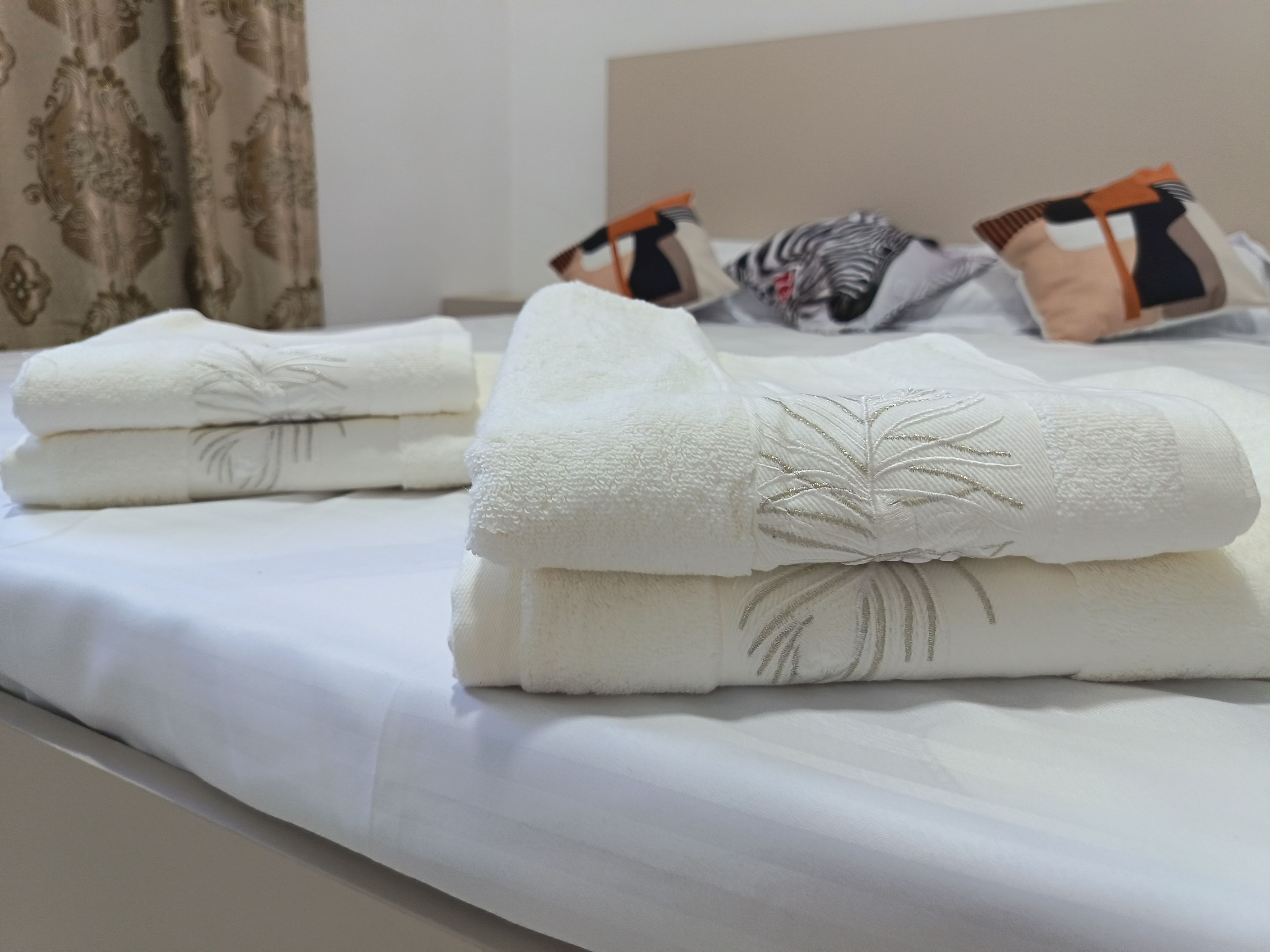 Ein ordentlich gemachtes Bett mit weißer Bettwäsche und einem Handtuch mit Palmenmotiv.