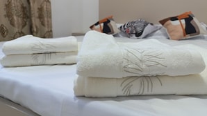 A neatly made bed with white bedding and a folded towel with a palm tree design. - Apartment Valley of legends mall  (Namangan)