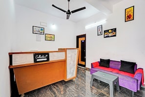 A reception area with a wooden desk, a couch, and artwork on the walls. - Collection O Ambattur Near Patravakam (Chennai)