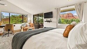 Une chambre d’hôtel avec un grand lit, un bureau avec une chaise, un téléviseur fixé au mur et une fenêtre donnant sur des formations rocheuses rouges.