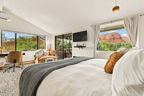 Habitación de hotel con una cama grande, un escritorio con silla, un televisor montado en la pared y una ventana con vistas a formaciones rocosas rojas.