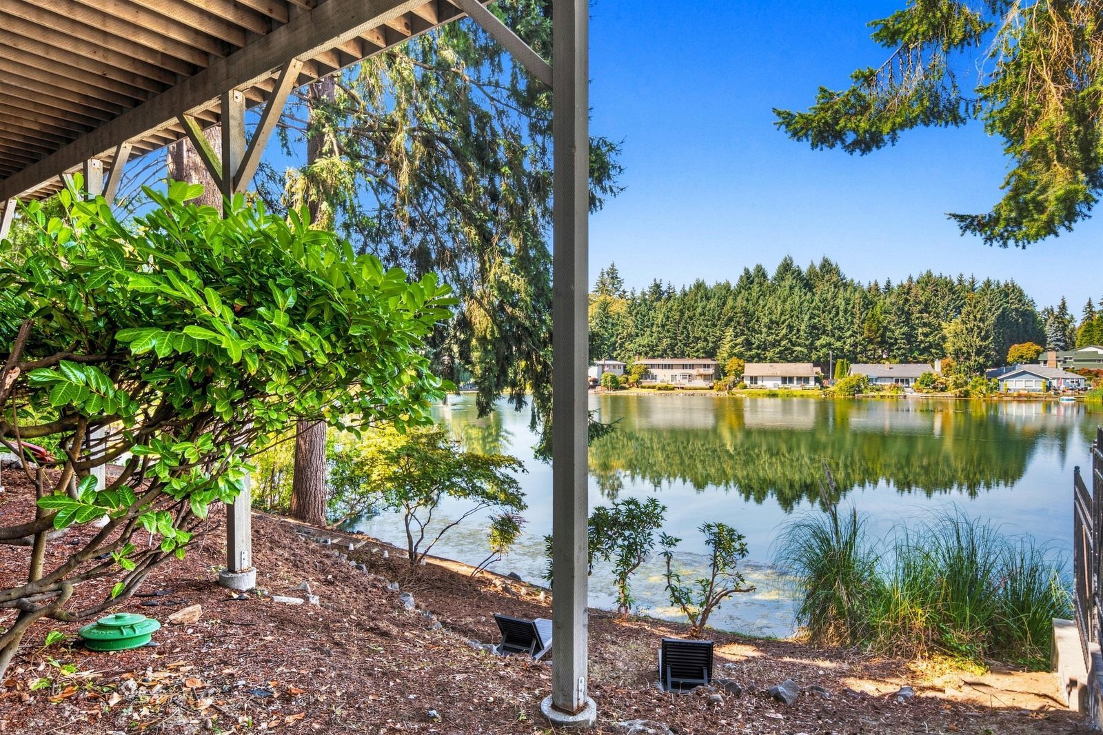 Un entorno tranquilo junto al lago, con una terraza de madera, un espacio cubierto y vistas a la orilla arbolada.