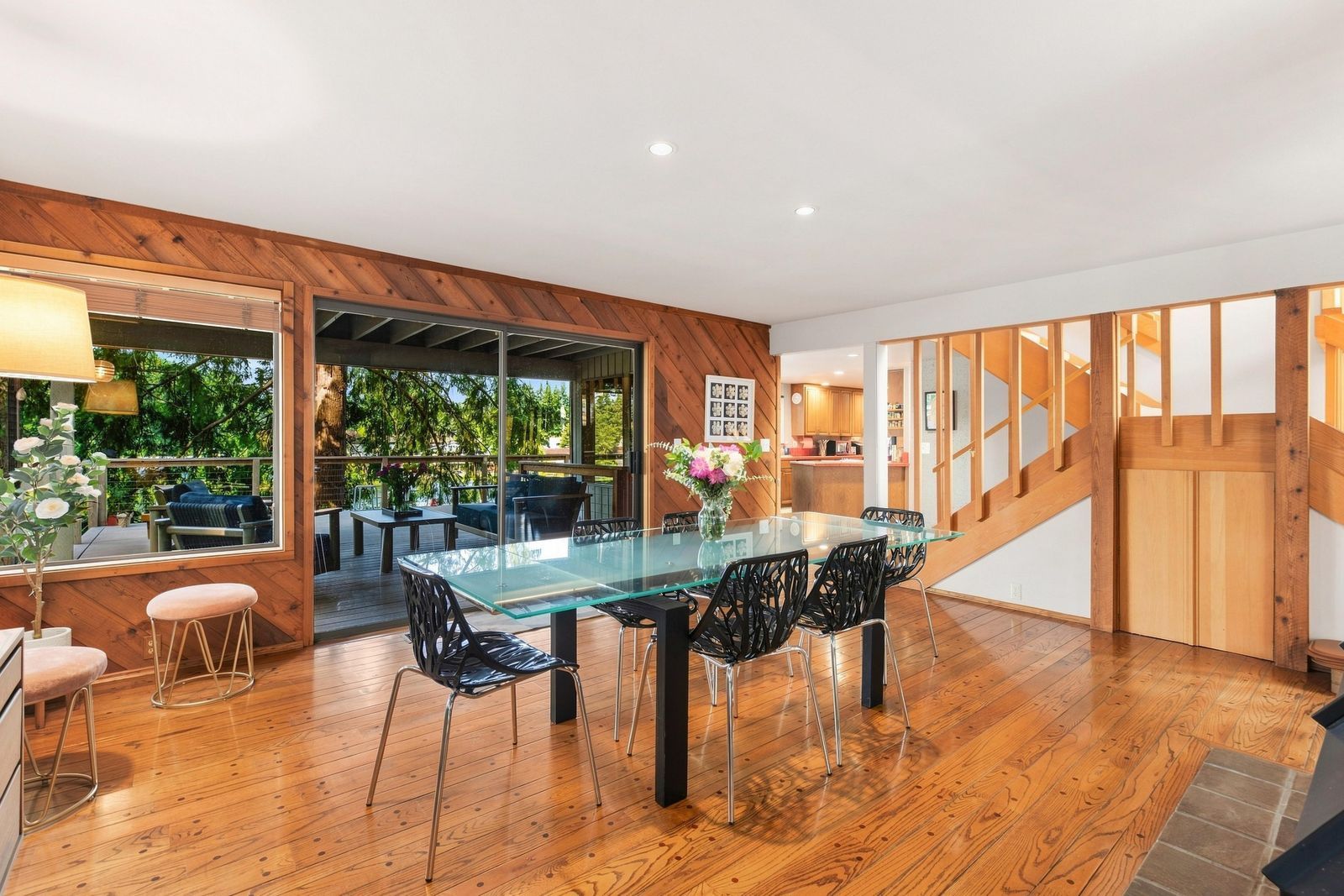 A modern dining area with a glass table, black chairs, and a wooden deck.