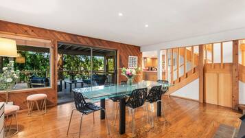 A modern dining area with a glass table, black chairs, and a wooden deck.