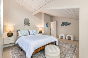 A bedroom with a bed, bedside lamps, a rug, a bench, and wall decor.