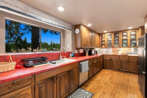 A modern kitchen with wooden cabinets, a red countertop, and a view of trees through a large window.