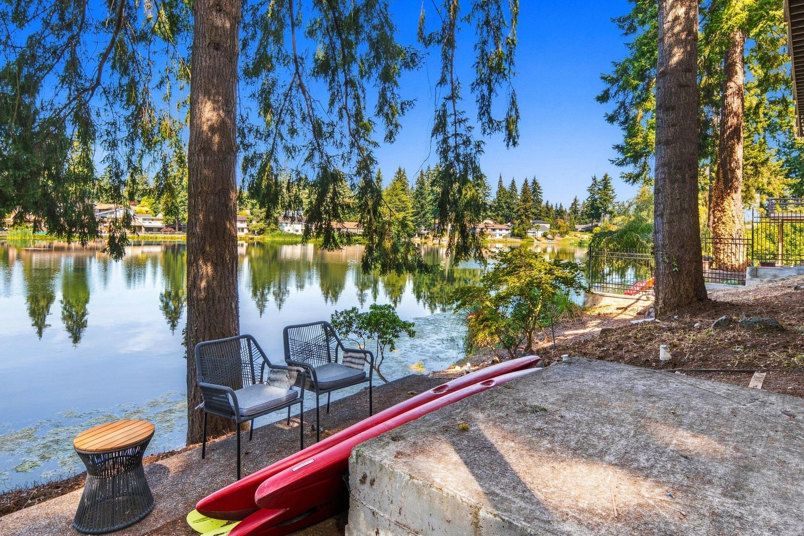 A lakeside seating area with chairs and a table, surrounded by trees and a calm lake.