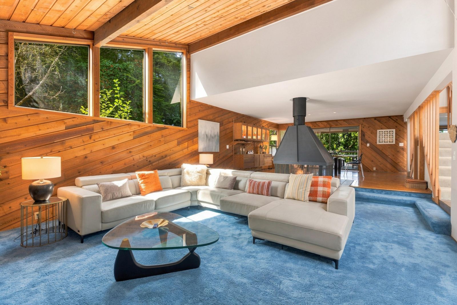 A modern living room with a sectional sofa, a glass coffee table, and a fireplace.