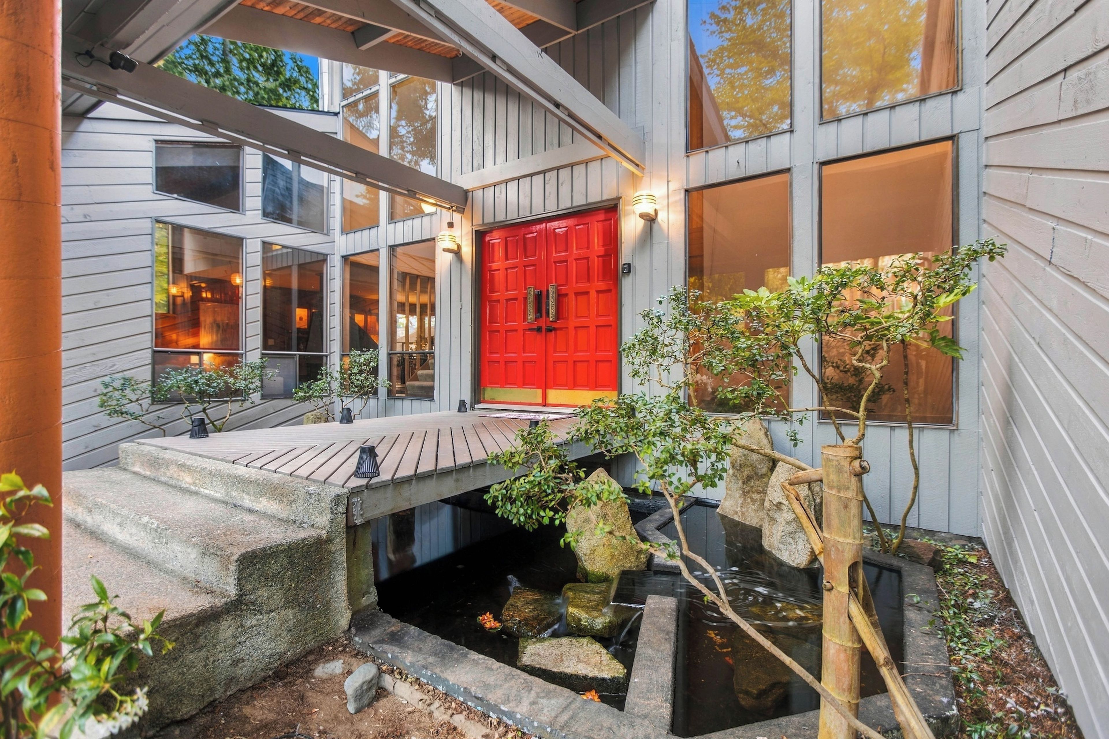 A modern house with a red door, a small pond, and a wooden deck.