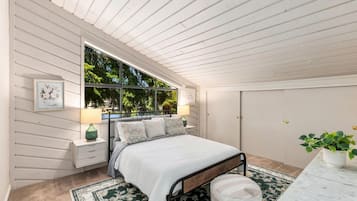A bedroom with a bed, nightstands, a window, a wardrobe, and a potted plant.