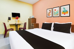 Hotellihuone, jossa on sänky, työpöytä, tuoli, televisio ja kolme kehystettyä taideteosta seinällä.