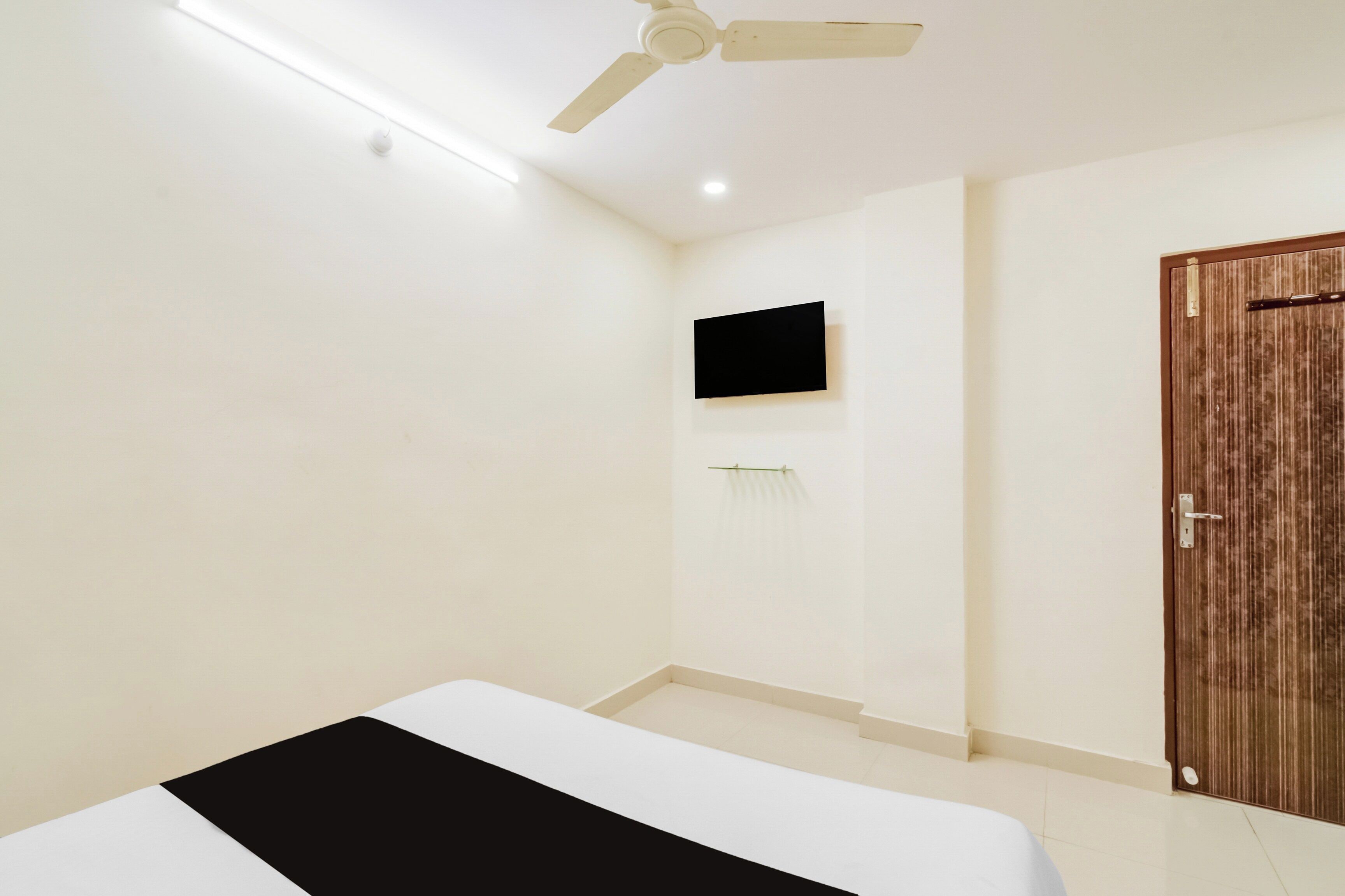 Habitación de hotel con cama, ventilador de techo, televisor montado y puerta de madera.