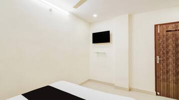Habitación de hotel con cama, ventilador de techo, televisor montado y puerta de madera.
