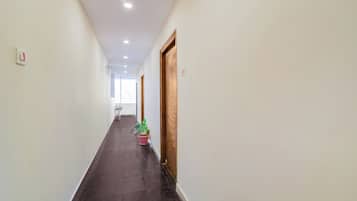 Un lungo e stretto corridoio con pavimento scuro, pareti bianche e una porta in legno sulla destra.