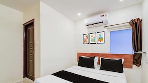 Una habitación de hotel con una cama, un ventanal con cortinas, un equipo de aire acondicionado y tres cuadros enmarcados en la pared.