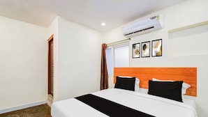 Una habitación de hotel con cama, ventana con cortinas, unidad de aire acondicionado y un cuadro colgado en la pared.