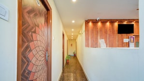 Un pasillo con una puerta de madera a la izquierda, un mostrador de recepción a la derecha y una planta en maceta en el centro.