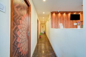 A hallway with a wooden door on the left, a reception desk on the right, and a potted plant in the middle. - Hotel O Neredmet Road (Hyderabad)