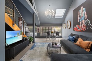 A modern living room with a flat-screen TV, a chandelier, a sofa with cushions, and artwork on the walls. - Harbourside 1-Bed Apt in Woolloomooloo Wharf (Woolloomooloo)