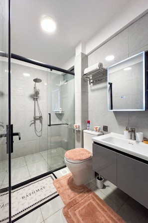 Une salle de bain moderne avec une douche à parois de verre, des toilettes avec un abattant rose et un meuble-lavabo avec un miroir.