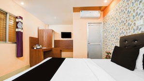 Hotellihuone, jossa on sänky, televisio, ilmastointilaite, vaatekaappi sekä pieni työpöytä, jossa on peili ja hygieniatarvikkeita.