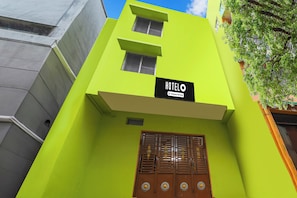 A building with a bright green facade, a sign reading 'HOTELO Company Serviced', and a traditional wooden door with decorative elements.