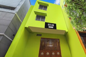 Un bâtiment à la façade d’un vert vif, une enseigne indiquant « HOTELO Company Serviced », et une porte en bois traditionnelle agrémentée d’éléments décoratifs.