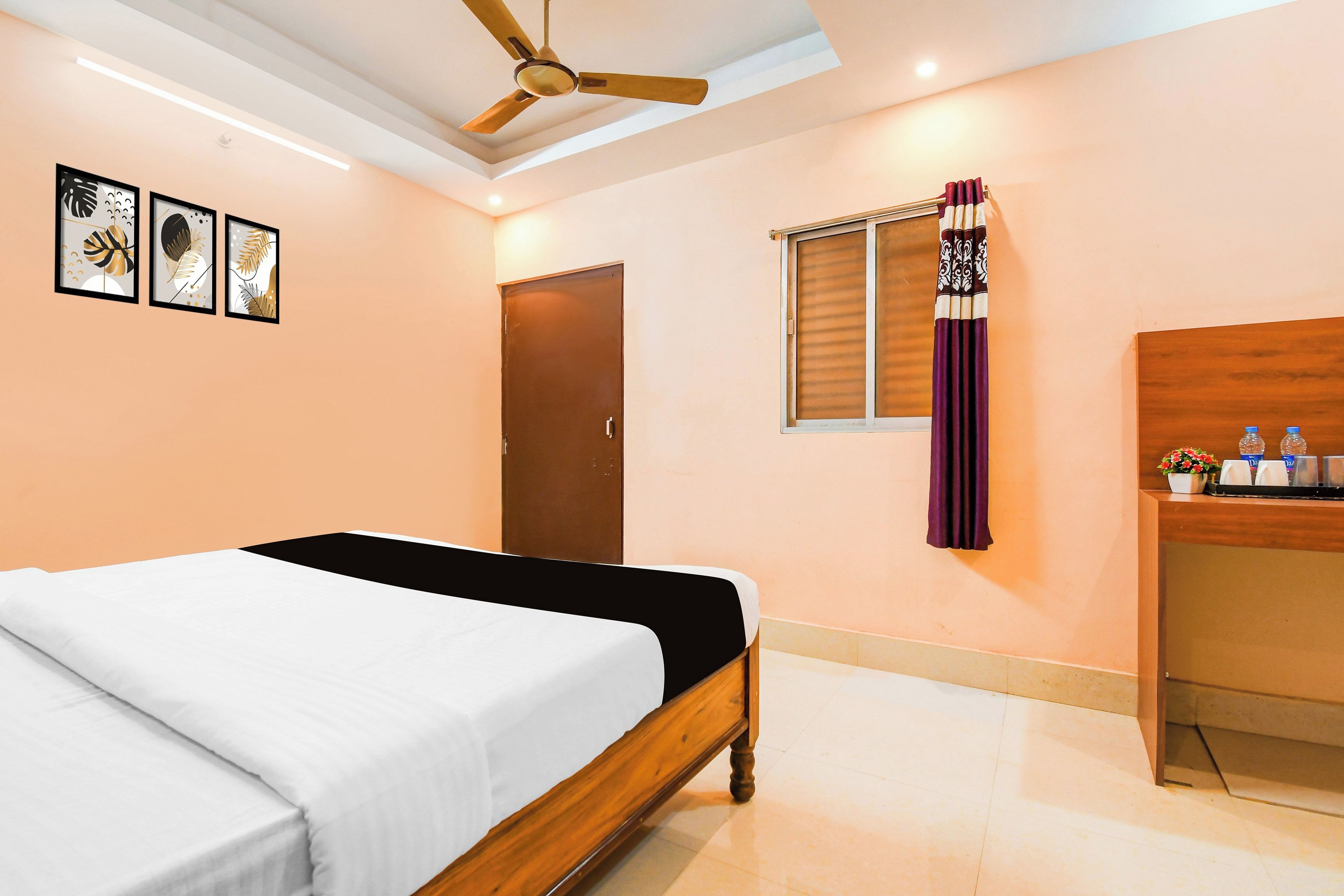 A bedroom with a bed, a ceiling fan, a door, a window with curtains, and a small desk with a mirror and toiletries.