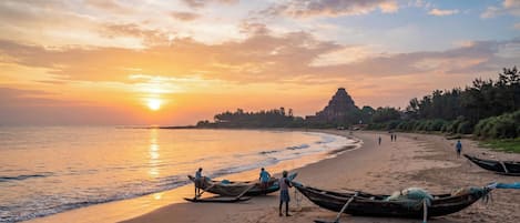 A beach with boats, a temple, and people walking.
