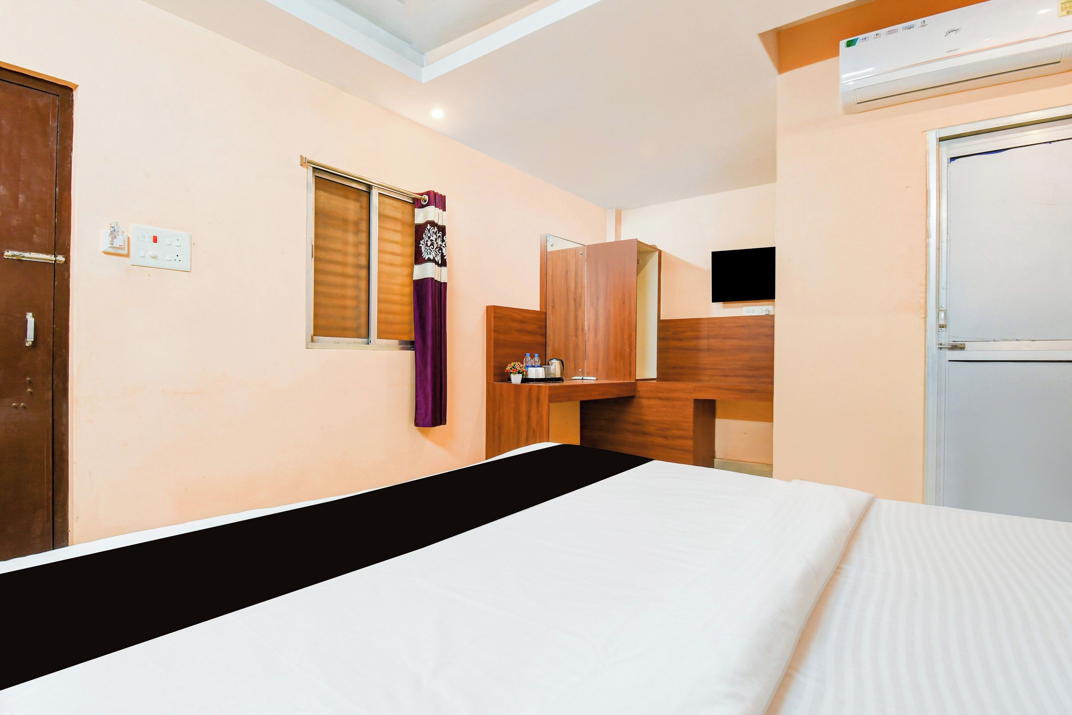 Une chambre d’hôtel avec un lit, une armoire en bois, une petite table avec une bouilloire et une fenêtre avec un rideau.