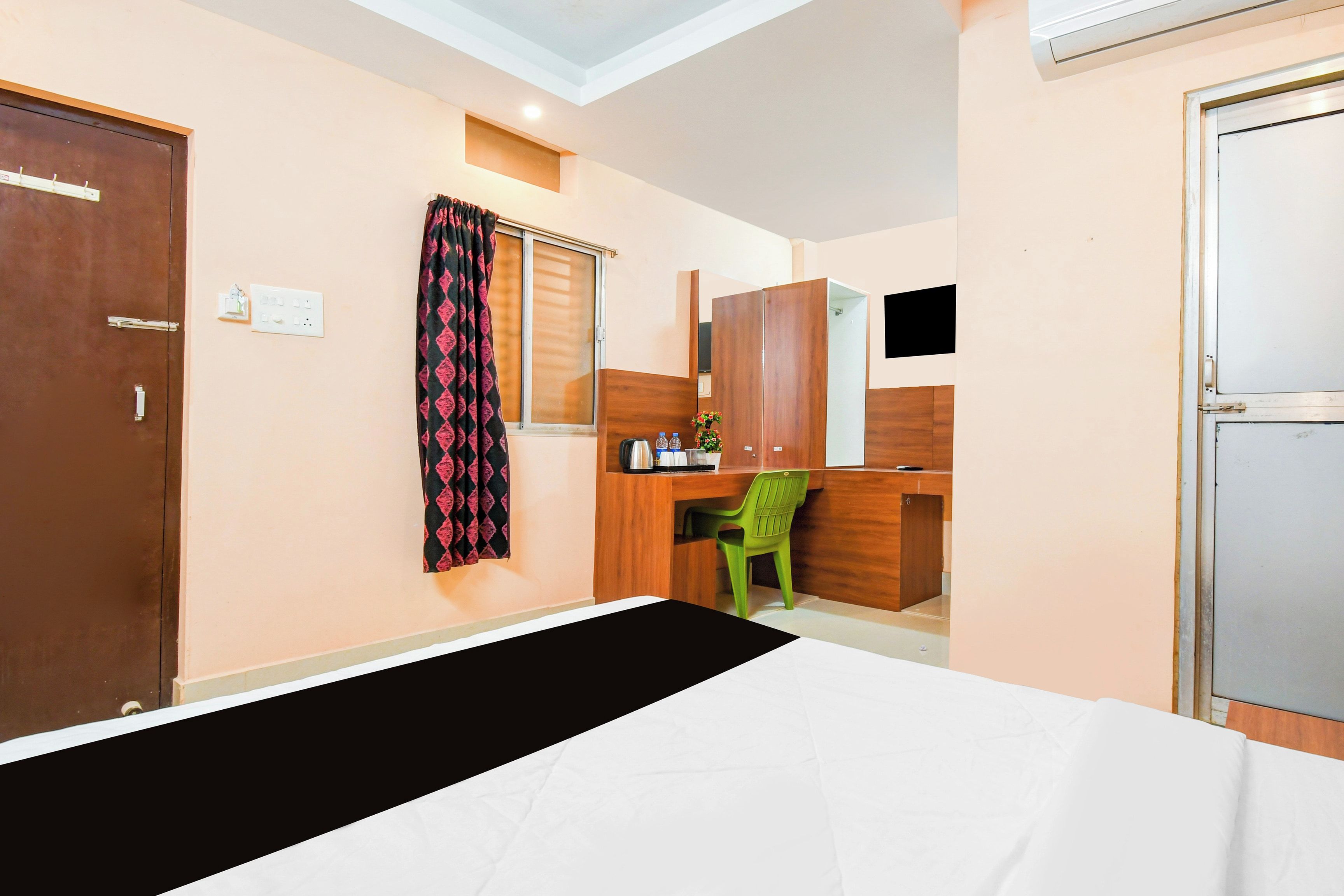Habitación de hotel con cama, escritorio, silla, armario y ventana con cortinas.