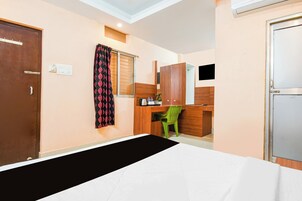 Une chambre d’hôtel comprenant un lit, un bureau, une chaise, une armoire et une fenêtre avec des rideaux.