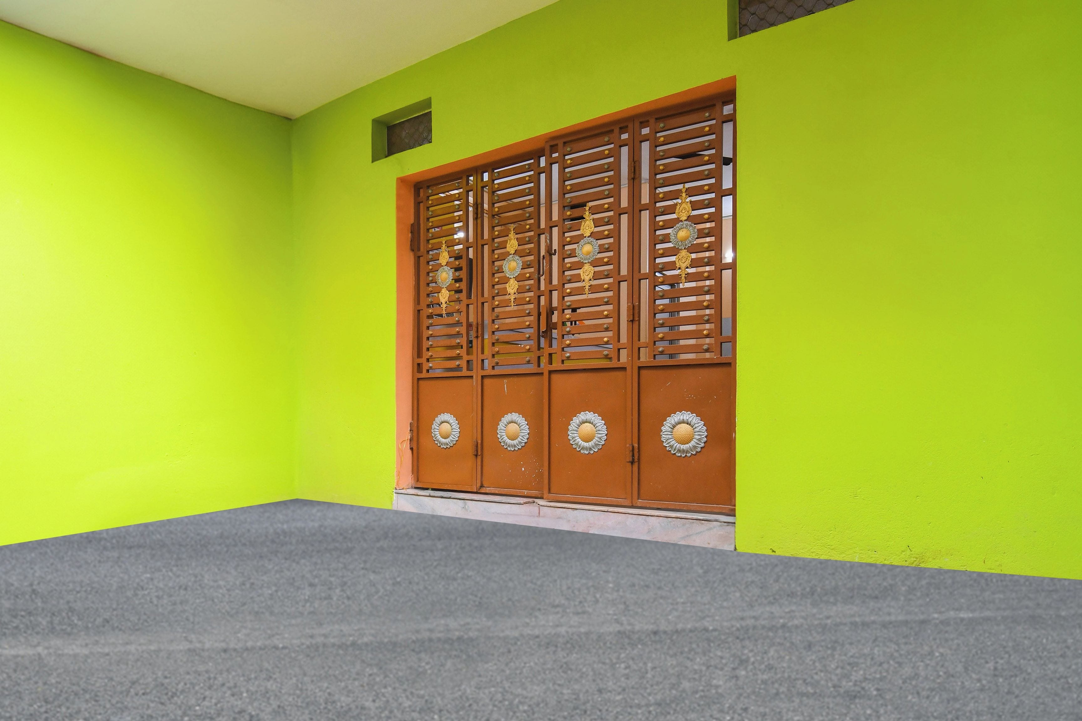 Una habitación con una pared verde brillante, piso alfombrado gris y una puerta de madera con detalles metálicos decorativos.